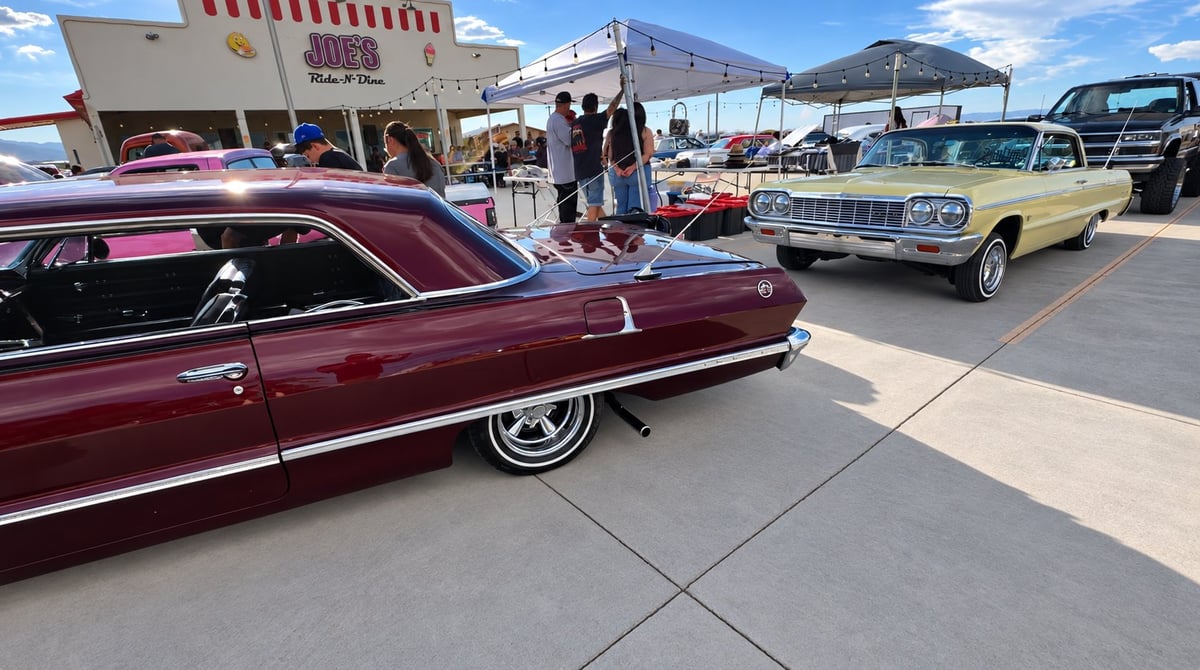 Classic cars on display at outdoor car show on sunny day with spectators and desert mountains