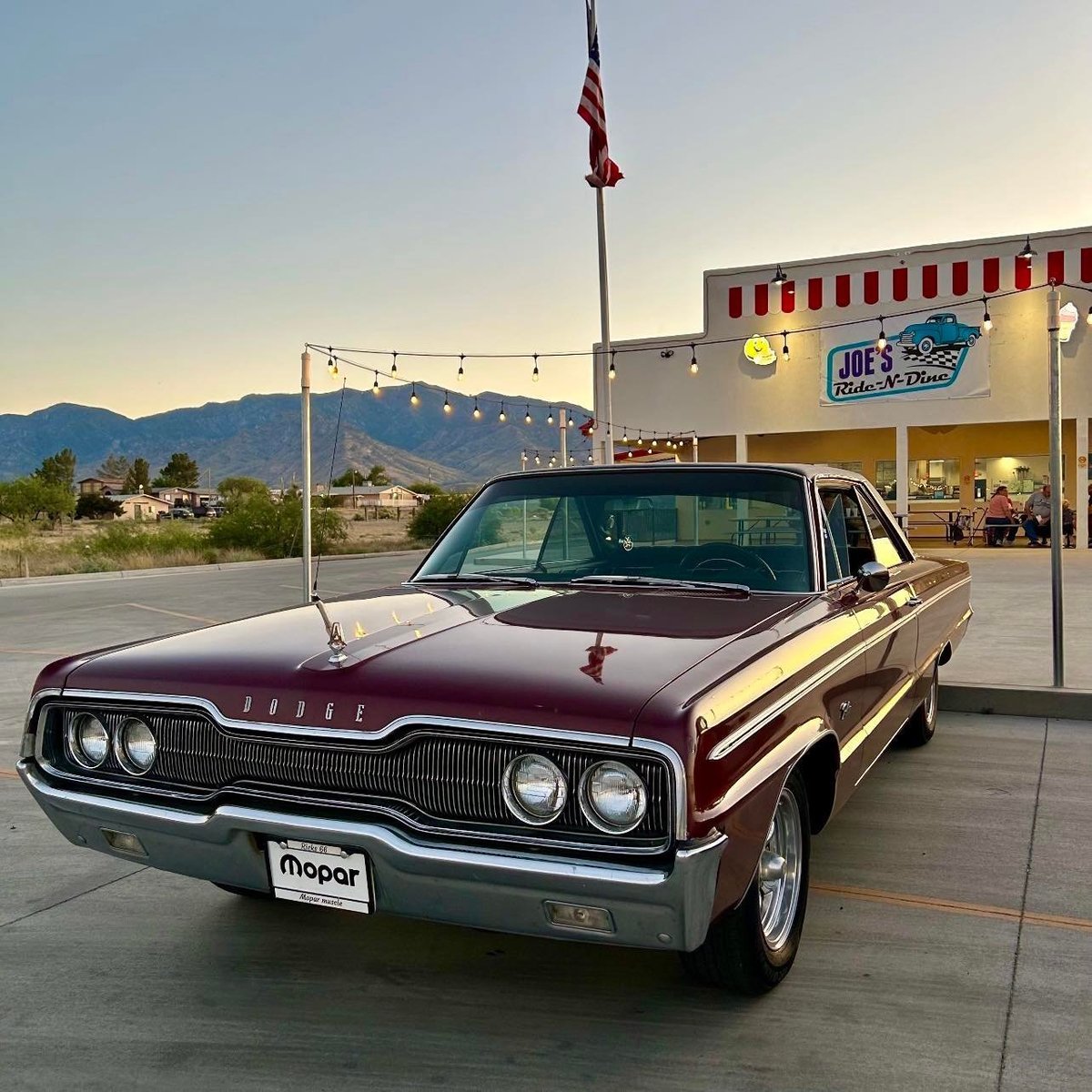 Maroon and cream 1960s Dodge Polara parked outside a retro diner with mountains in the background